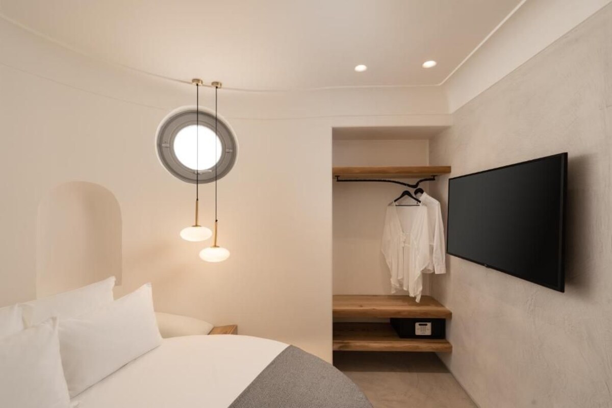 A modern hotel room with a bed, a round ceiling light, a TV mounted on the wall, and a walk-in closet.