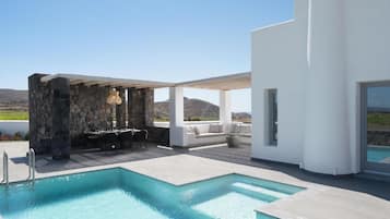 A pool area with a stone structure, seating, and a view of the landscape.