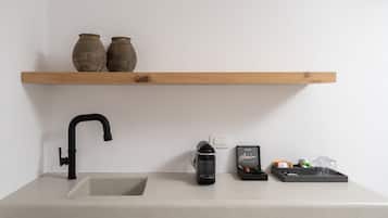 Uma cozinha com pia, cafeteira, prateleira com dois vasos e bandeja com copos e uma caixa.
