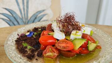 A glass plate with a salad consisting of tomatoes, avocado, and feta cheese, garnished with microgreens and a sprig of rosemary.