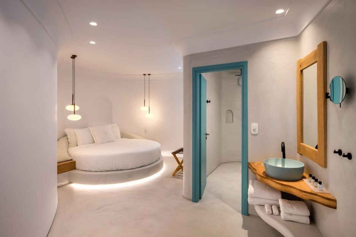 A modern bedroom with a circular bed, a wooden vanity with a round sink, and a large mirror.