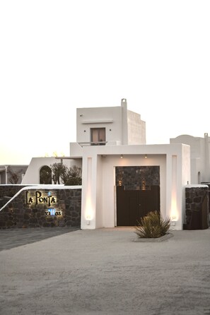 A building with a stone wall, a large dark door, and a sign that reads 'La Ponta.' - La Ponta Villas&suites (Santorini)