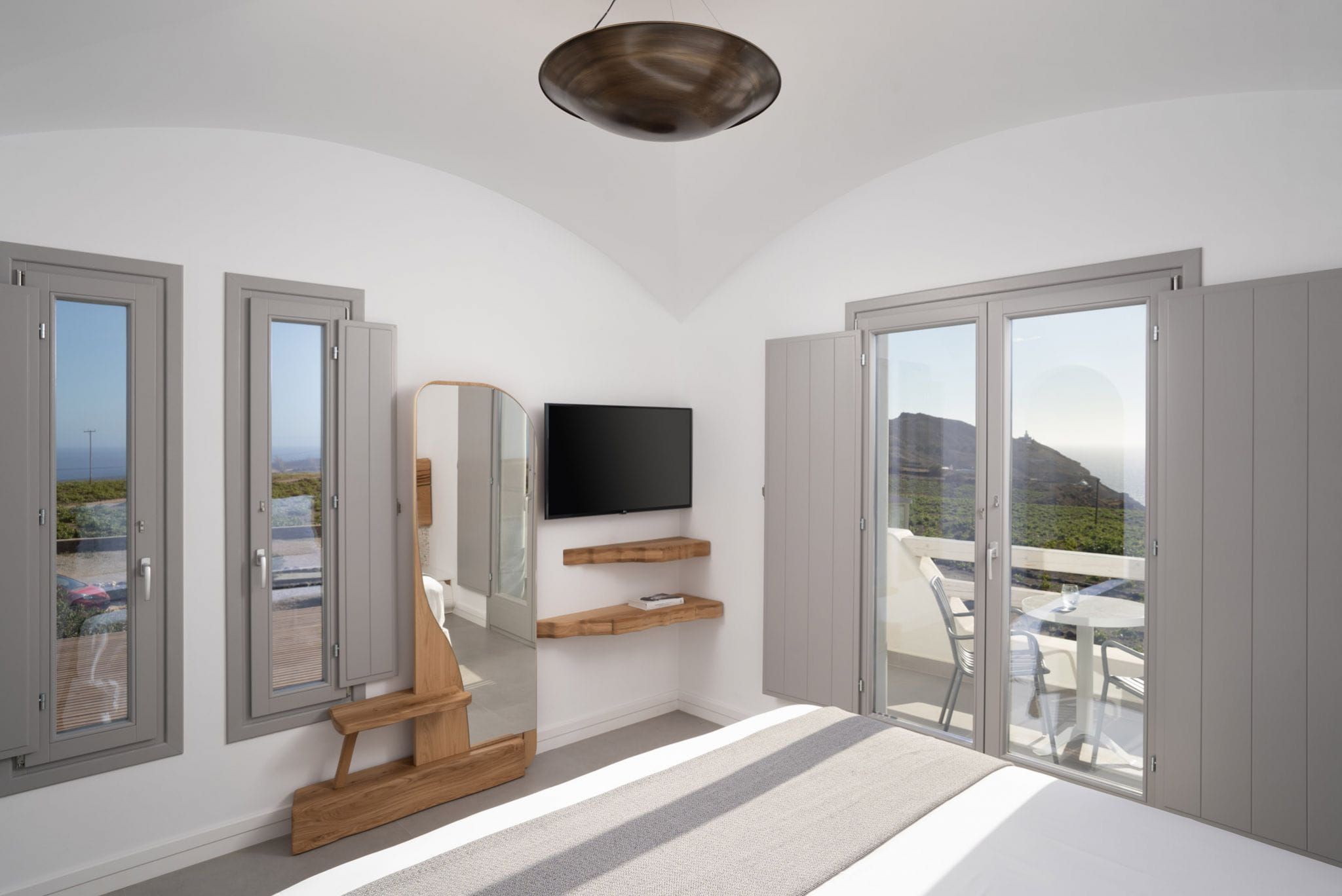 A modern bedroom with a TV, wooden bench, and a balcony with a table and chairs.