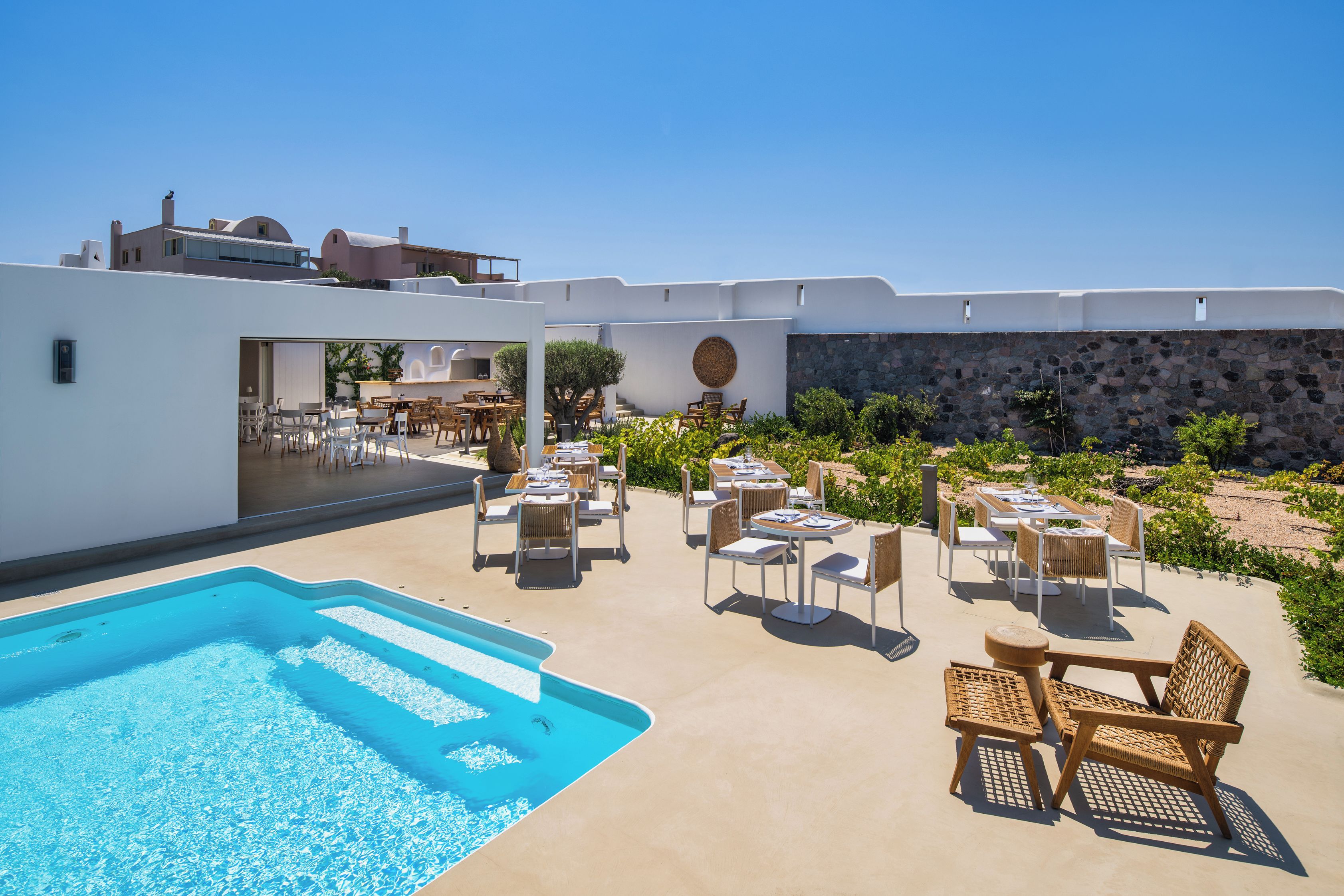 A poolside area with lounge chairs and tables, a swimming pool, and a view of buildings in the background.