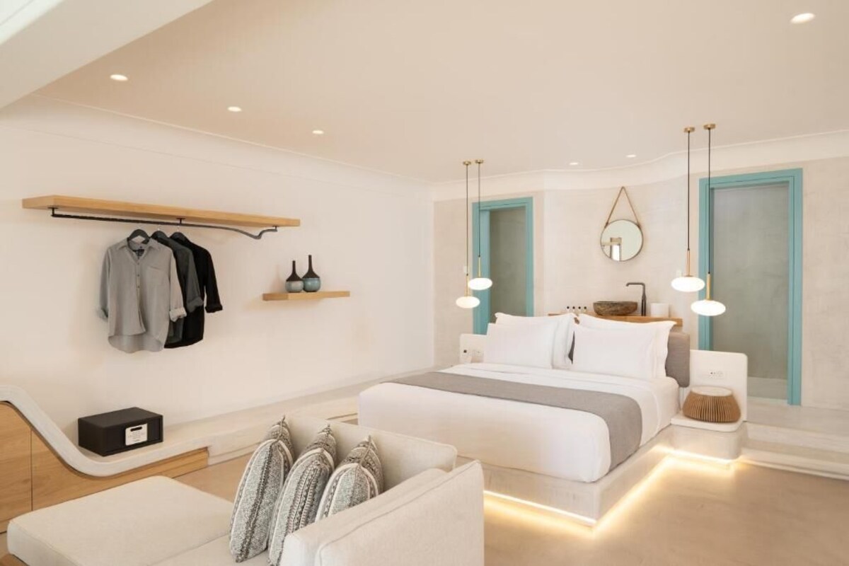 Un dormitorio moderno con una cama, mesitas de noche, una lámpara colgante, un espejo y un perchero con ropa.