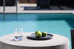 A poolside table with a glass of water and two limes. - La Ponta Villas&suites (Santorini)