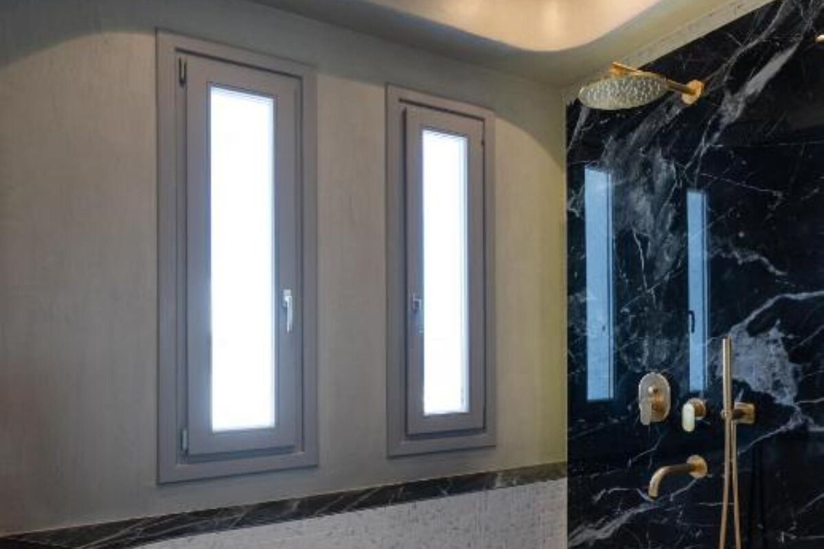 Un baño con una bañera independiente, ducha con pared de mármol y dos ventanas con vidrio esmerilado.