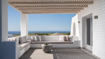 Un balcón moderno con fachada blanca, una zona de estar integrada con cojines y vistas al mar.