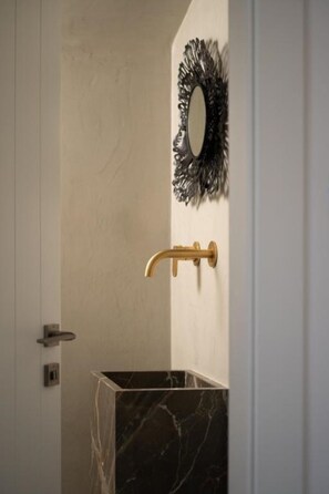A bathroom with a marble sink, a gold faucet, and a decorative mirror. - La Ponta Villas&suites (Santorini)