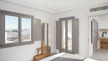 Un dormitorio con un ventanal grande, un banco de madera, un espejo y un baño con lavabo.
