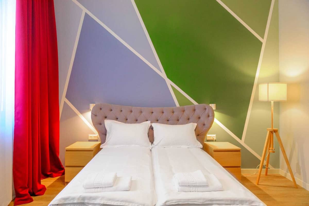 Un lit double avec du linge de lit blanc, une tête de lit capitonnée et une lampe de chevet.