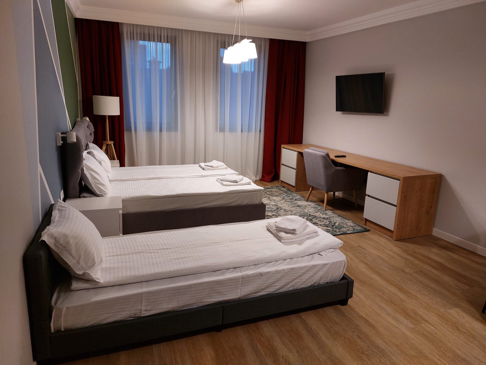 Habitación de hotel con dos camas, un escritorio, una silla, televisión y ventana con cortinas.