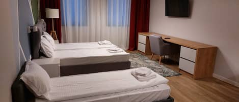 Habitación de hotel con dos camas, un escritorio, una silla, televisión y ventana con cortinas.