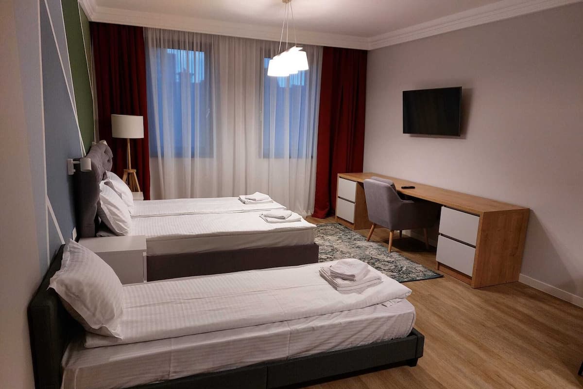 Une chambre d’hôtel avec deux lits, un bureau, une chaise, une télévision et une fenêtre avec des rideaux.