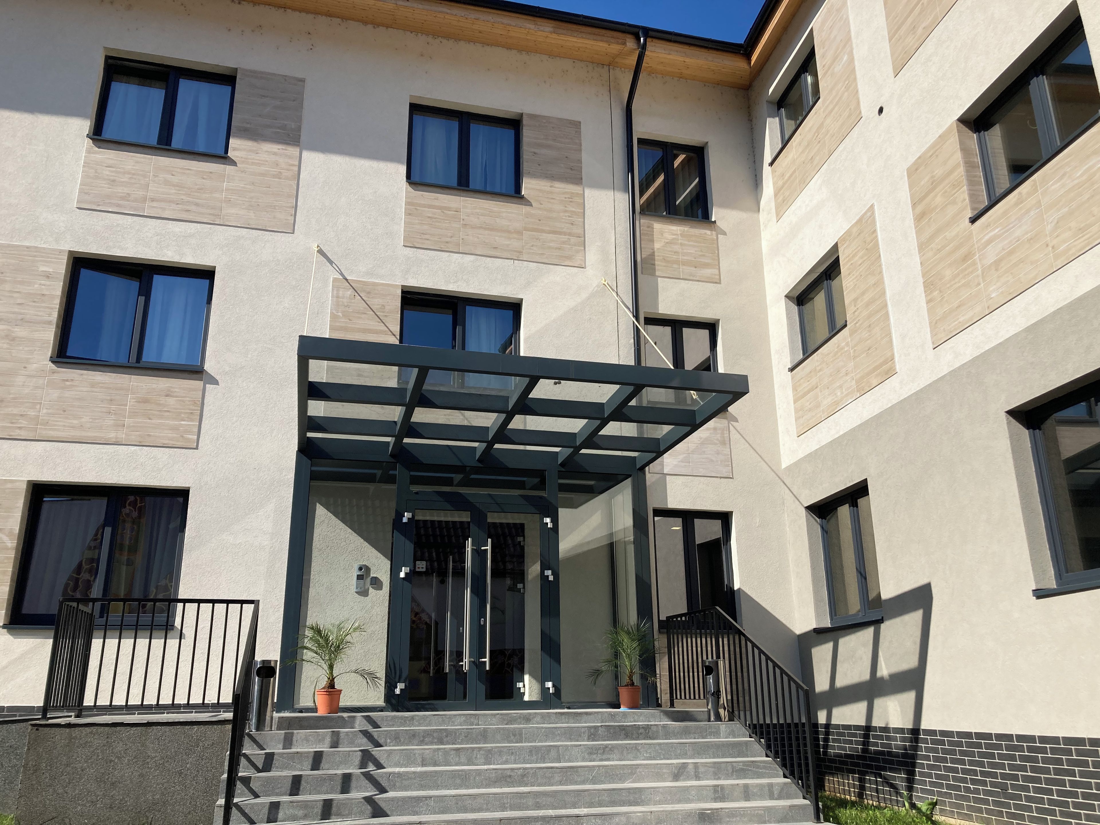 A modern building with a covered entrance, multiple windows, and a staircase leading to the entrance.
