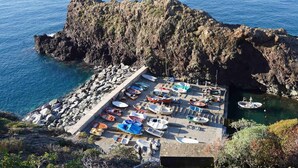 Une zone côtière rocheuse avec un quai rempli de petits bateaux et une falaise rocheuse en arrière-plan.