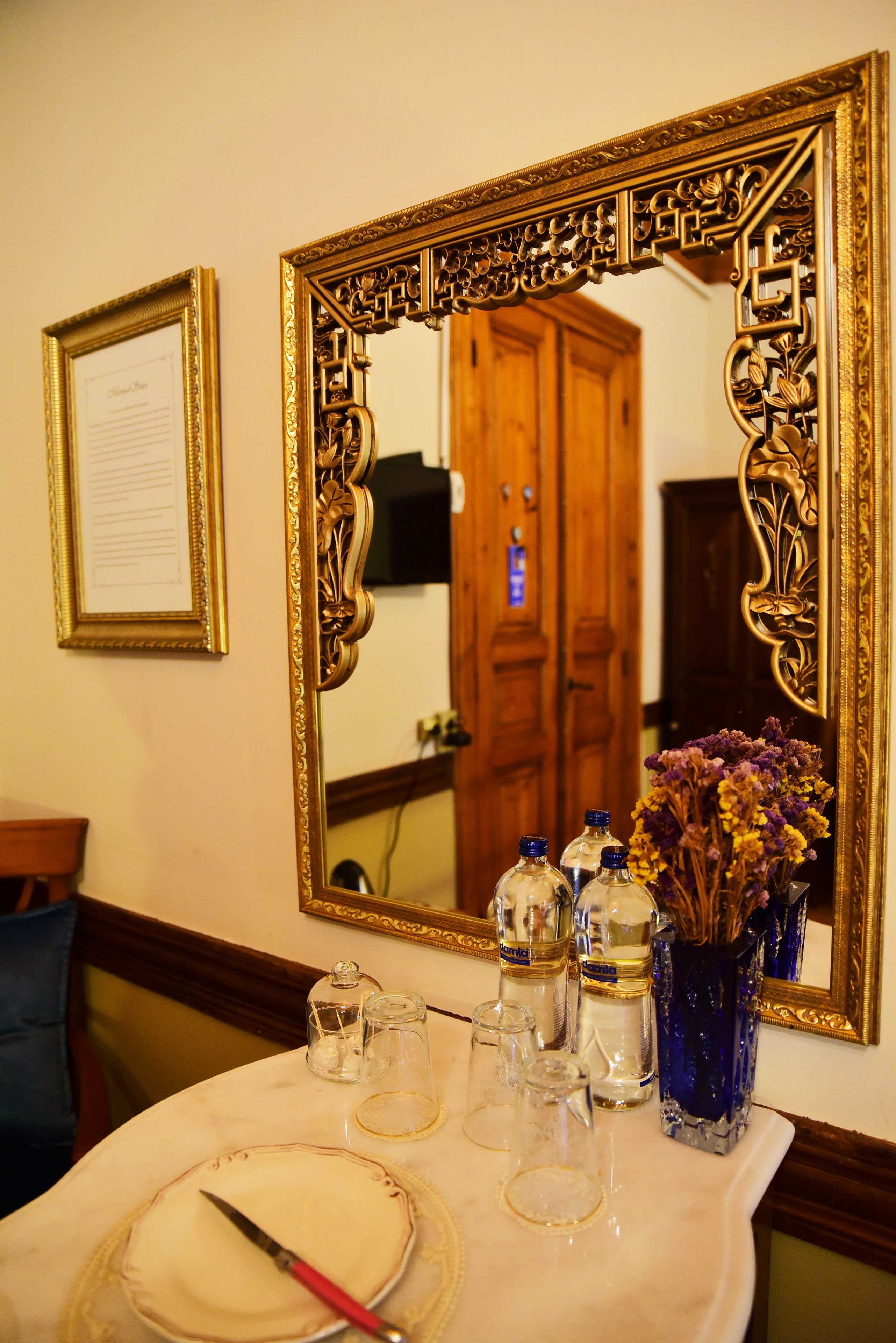 A table with a mirror, a framed certificate, and a vase with dried flowers.