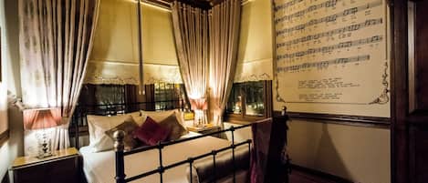 A room with a bed, curtains, a nightstand, a lamp, a window, and a wall with a musical score.