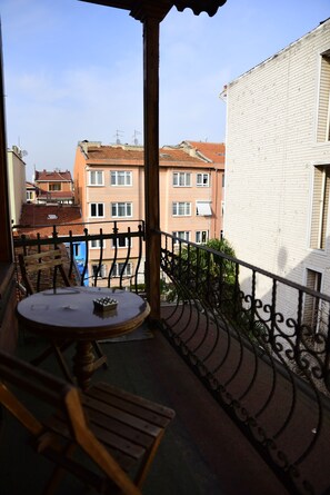 Een balkon met een tafel en stoelen, een ijzeren hekwerk en gebouwen op de achtergrond.