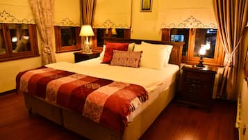 A hotel room with a large bed, two bedside tables with lamps, a wooden dresser, and curtains on the windows.
