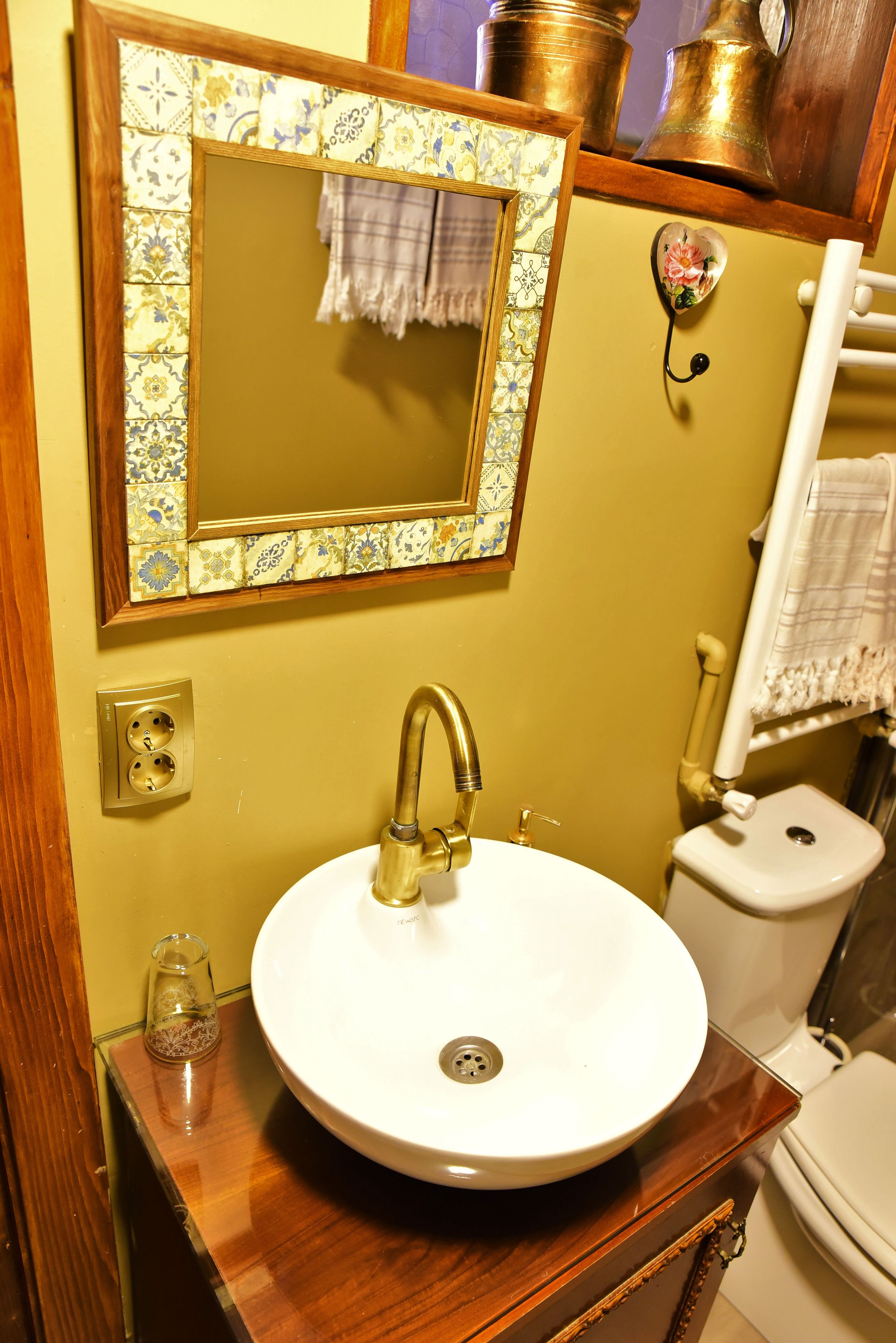 A bathroom with a round sink, a mirror with a decorative frame, a toilet, and a towel rack.