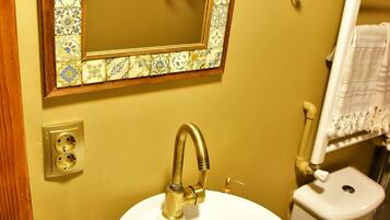 A bathroom with a round sink, a mirror with a decorative frame, a toilet, and a towel rack.