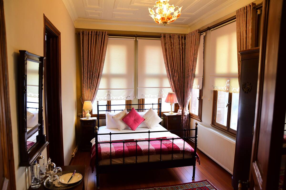 Un dormitorio con cama, mesitas de noche, un espejo, cortinas y un candelabro.