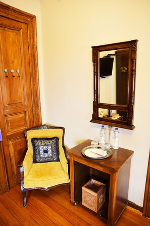 Une porte en bois, une chaise avec un coussin à motifs, une petite table en bois avec un miroir et une poubelle.