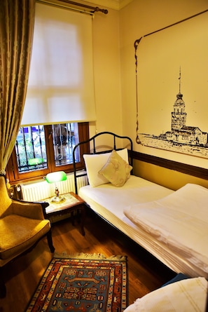 Una habitación con una cama, una silla, una mesa con lámpara, una ventana con cortinas y un mural de un faro en la pared.