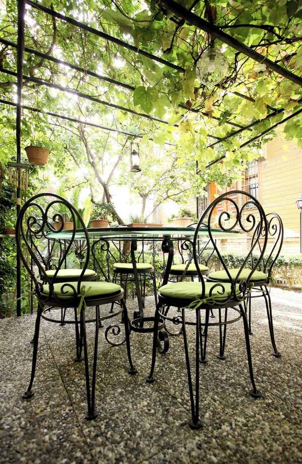 Un patio con una mesa y sillas, rodeado de follaje y un edificio al fondo.