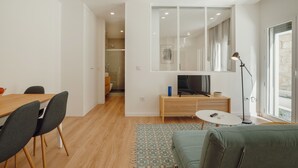 A modern living room with a sofa, a dining table with chairs, a TV, and a lamp. - Apartment  by Interhome (Porto)