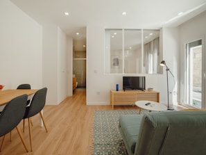 A modern living room with a sofa, a dining table with chairs, a TV, and a lamp. - Apartment  by Interhome (Porto)