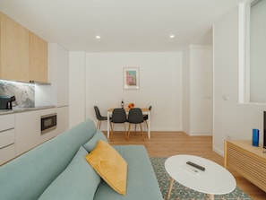 A modern living room with a sofa, a dining table with chairs, a kitchen area, and a small TV stand. - Apartment  by Interhome (Porto)