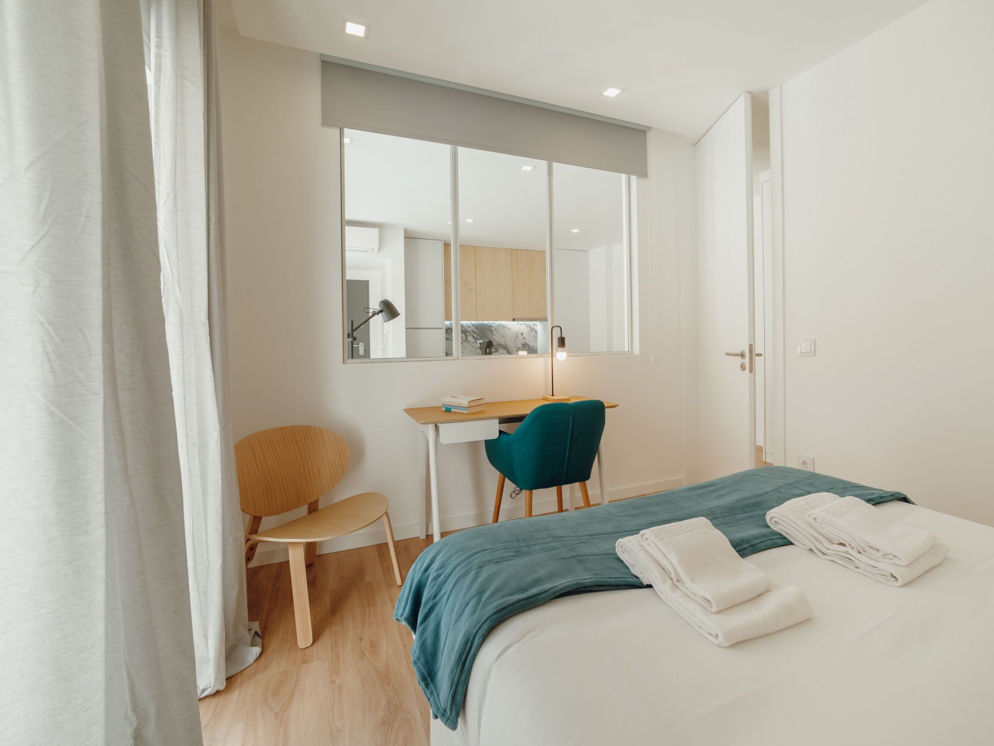 Une chambre d’hôtel avec un lit, un bureau, une chaise, un miroir et une porte.