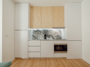A compact kitchen with white cabinets, a marble countertop, a coffee maker, and a built-in oven. - Apartment  by Interhome (Porto)