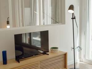 A modern living room with a flat-screen TV on a wooden cabinet, a floor lamp, and a small table with a cup. - Apartment  by Interhome (Porto)