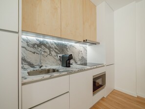 A modern kitchen with a marble countertop, a coffee machine, a built-in oven, and wooden cabinets. - Apartment  by Interhome (Porto)