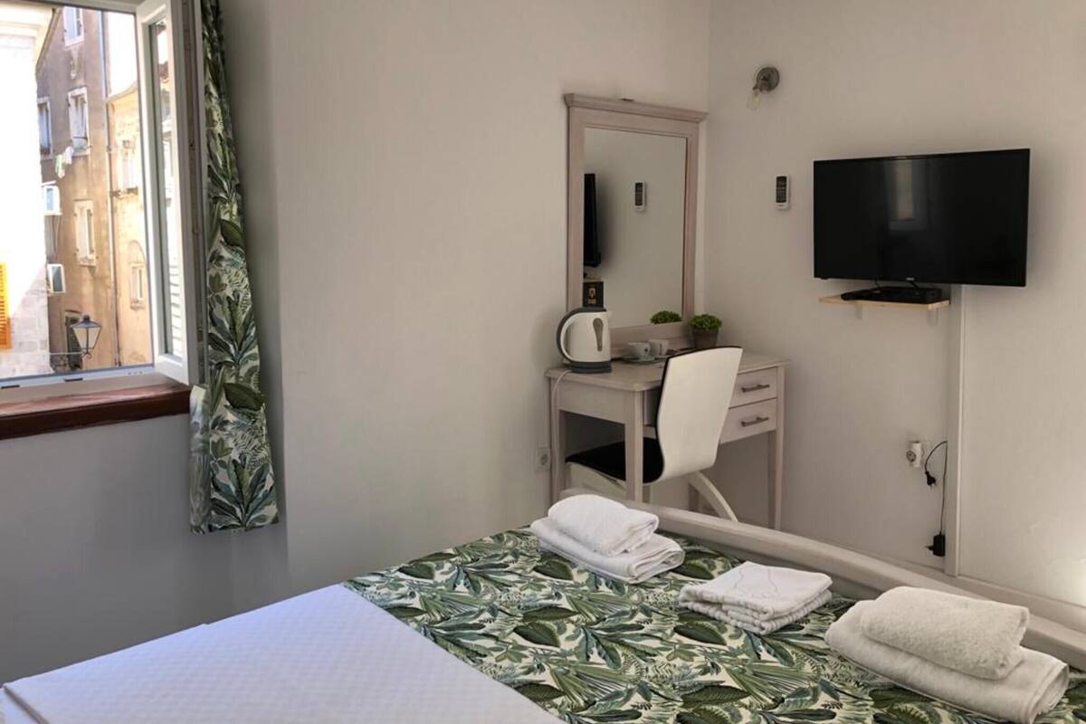Une chambre d’hôtel comprenant un lit, un bureau avec une chaise, une télévision et une fenêtre avec des rideaux.