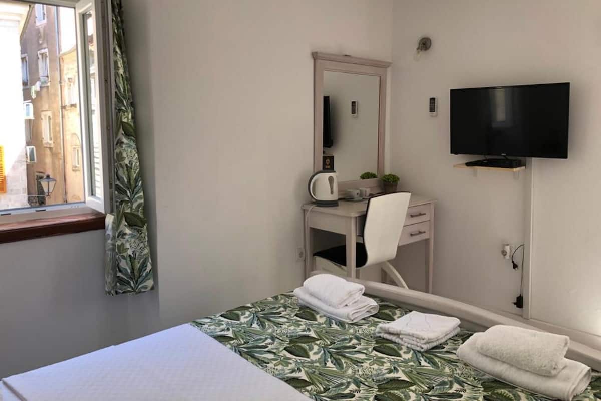 A hotel room with a bed, a desk with a chair, a television, and a window with curtains.