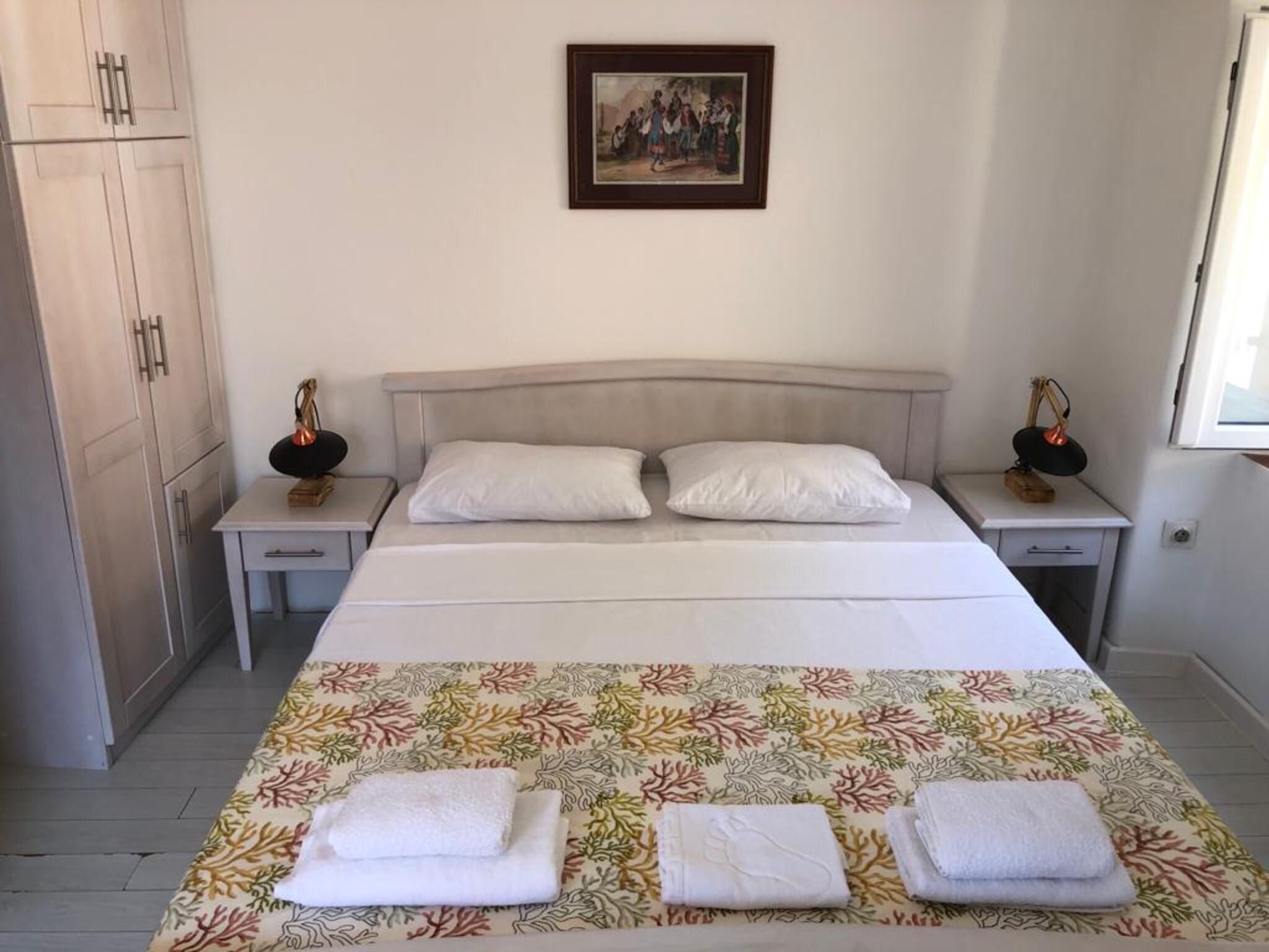 A bedroom with a bed, two nightstands, a wardrobe, a framed picture on the wall, and a window.