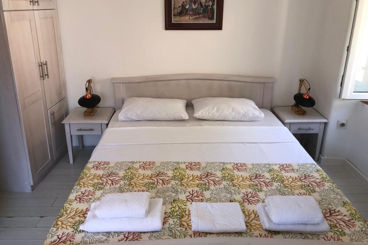 A bedroom with a bed, two nightstands, a wardrobe, a framed picture on the wall, and a window.