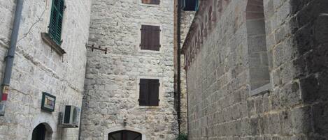 Une étroite ruelle pavée bordée d’un bâtiment dont la façade est ornée d’une porte d’entrée en arc de cercle au centre et de plusieurs fenêtres.