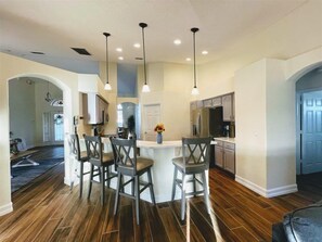 A modern kitchen with a central island, bar stools, pendant lighting, and a view into the dining area. - Orange Tree Executive Gameroom (Davenport)
