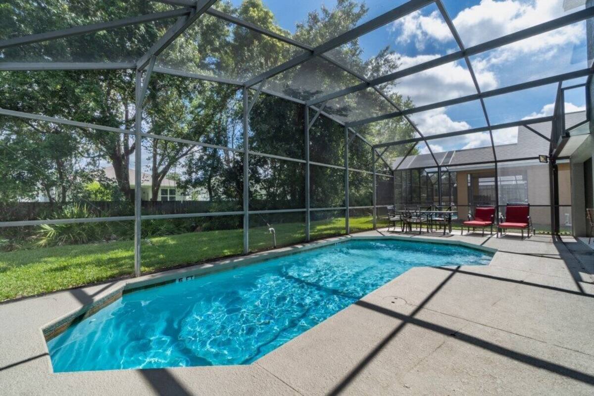 A covered outdoor swimming pool with a clear view of the surrounding greenery and a covered seating area.