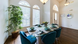 Comedor con mesa lista para cuatro personas, una planta grande en maceta y vistas al exterior.