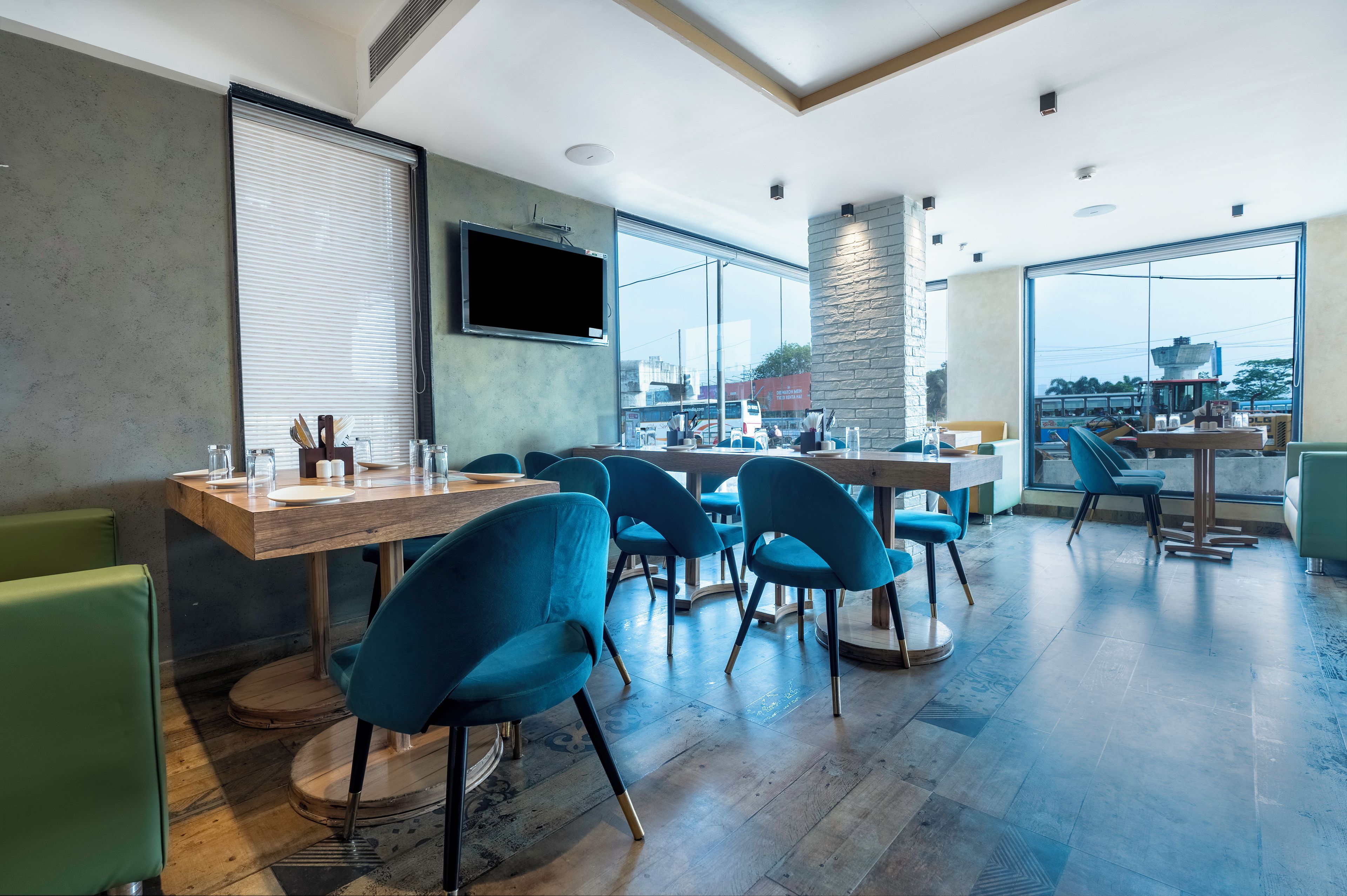A modern dining area with wooden tables, blue chairs, and large windows offering a view of the city.