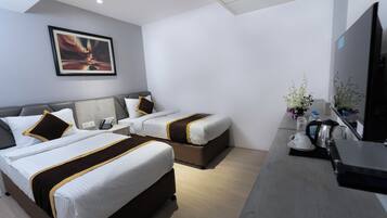 A hotel room with two beds, a desk with a kettle, a TV, and a framed picture on the wall.