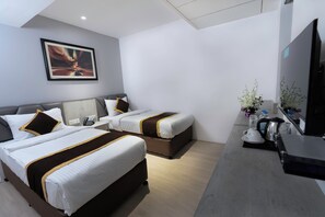 Habitación de hotel con dos camas, un escritorio con hervidor, un televisor y un cuadro en la pared.