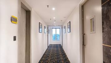 A hallway with a patterned carpet, framed pictures on the walls, and a door with a number sign.