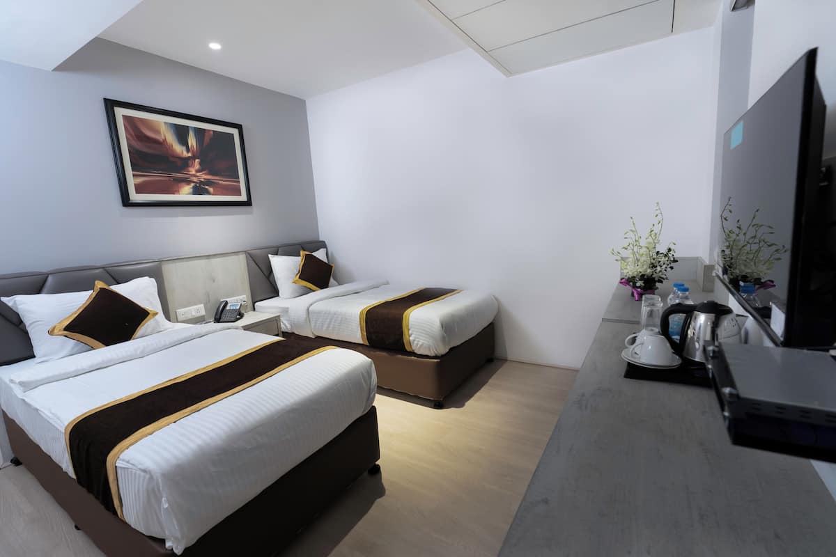 Een hotelkamer met twee bedden, een bureau met waterkoker, een televisie en een ingelijst foto aan de muur.